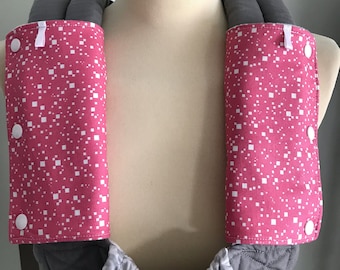May include: A pair of pink and white patterned fabric shoulder pads with white buttons. The shoulder pads are attached to a gray fabric carrier.