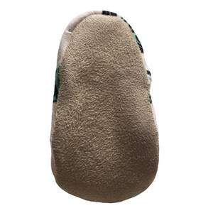 May include: A close-up of the bottom of a slipper with a brown fuzzy sole and a green and white patterned fabric top.