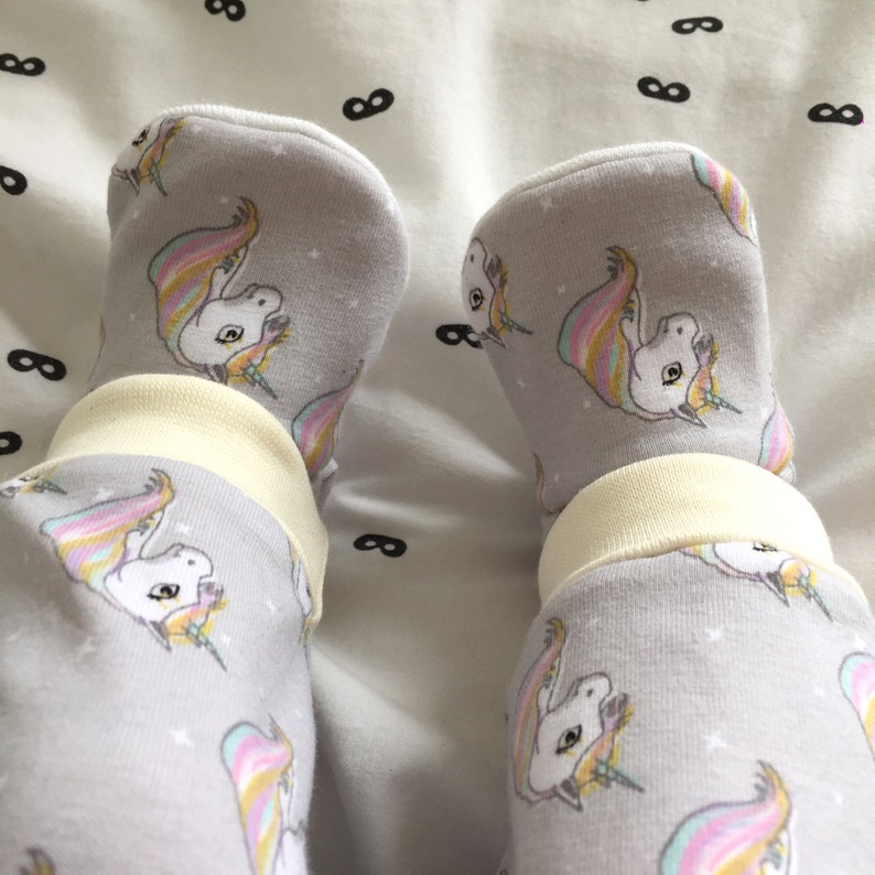 May include: Gray baby leggings with a unicorn print. The leggings have a white cuff at the ankle and feature a rainbow unicorn design.