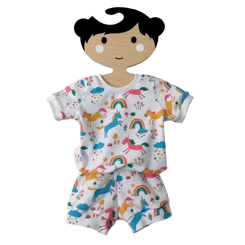 May include: White short-sleeved shirt and matching shorts with a colorful unicorn print. The shirt has a round neckline and the shorts have an elastic waistband.