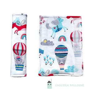 May include: A set of two fabric car seat belt covers featuring a whimsical unicorn, hot air balloons, and a cute bear. The covers are white with colorful illustrations and the text "Unicorn Balloons".