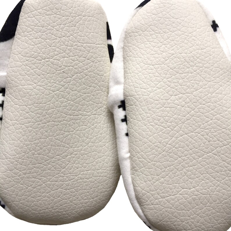 May include: Close-up of the bottom of a pair of white and black slippers. The slippers have a textured white sole.