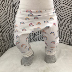 Op de afbeelding: Witte baby leggings met een regenboogpatroon. De leggings zijn gemaakt van een zachte, rekbare stof en hebben een comfortabele pasvorm.
