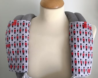 May include: A pair of gray baby carrier shoulder pads with a red and black print of a repeating pattern of a soldier holding an umbrella. The shoulder pads are made of a soft, padded material.