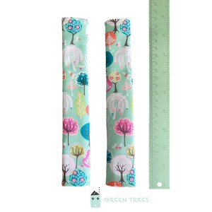 May include: Two fabric seat belt covers with a colorful tree pattern on a light green background. The pattern includes pink, blue, orange, and white trees. A green ruler is next to the covers. The text "GREEN TREES" is at the bottom.