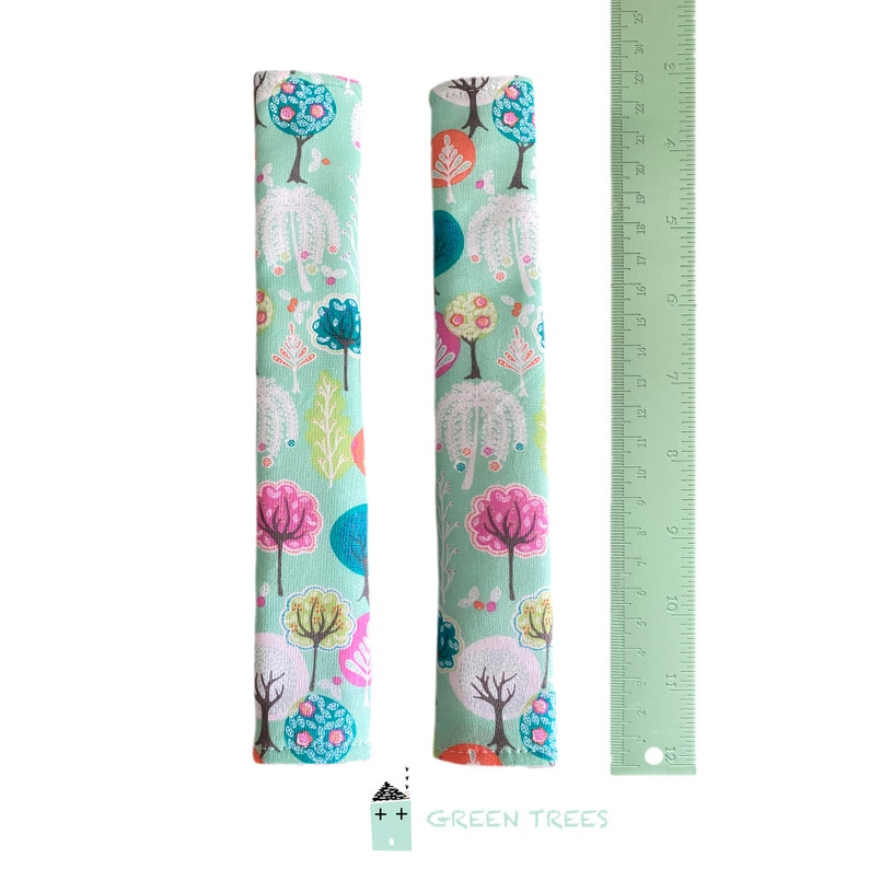 May include: Two fabric seat belt covers with a colorful tree pattern on a light green background. The pattern includes pink, blue, orange, and white trees. A green ruler is next to the covers. The text "GREEN TREES" is at the bottom.