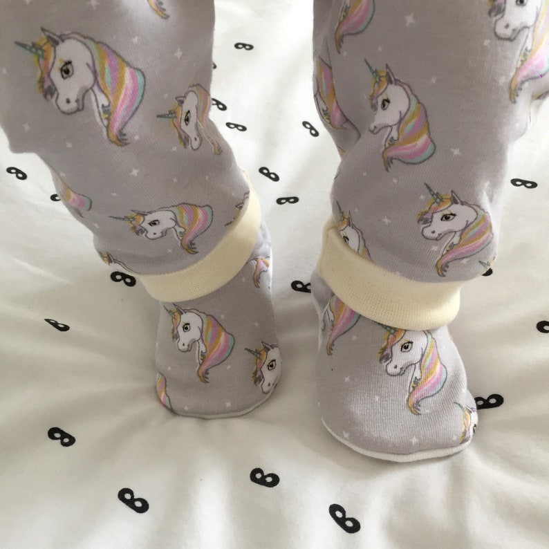 May include: Gray baby leggings with a unicorn print and white cuffs. The leggings are paired with gray baby booties with a unicorn print and white cuffs.
