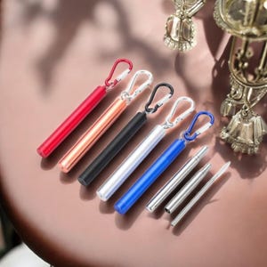 Op de afbeelding: Zes verschillende gekleurde metalen rietjes met een karabijnhaak. De rietjes zijn rood, koper, zwart, zilver, blauw en roestvrij staal. De rietjes zijn allemaal ongeveer 20 cm lang en perfect om mee te nemen.