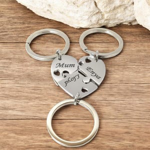 Può includere: Portachiavi a forma di cuore argentato con tre pezzi di puzzle che si incastrano. I pezzi sono incisi con i nomi "Mum", "Enya" e "PJ".