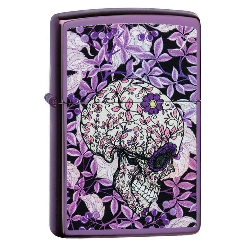 May include: Purple metal lighter with a floral skull design. The skull is decorated with pink and white floral patterns, set against a backdrop of purple leaves and berries. The lighter has a shiny, metallic finish.