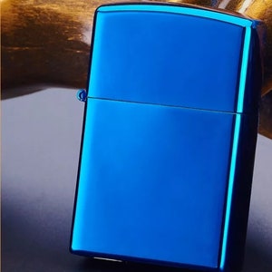 Op de afbeelding: Een blauwe metalen aansteker met een gladde, glanzende afwerking. De aansteker heeft een rechthoekige vorm met afgeronde hoeken.