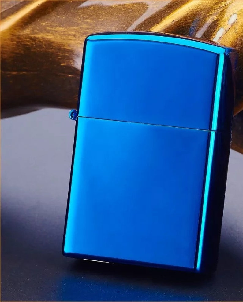 Op de afbeelding: Een blauwe metalen aansteker met een gladde, glanzende afwerking. De aansteker heeft een rechthoekige vorm met afgeronde hoeken.