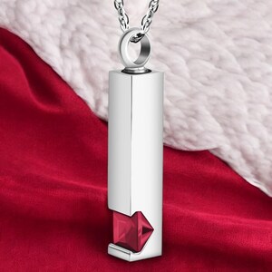 May include: Silver pendant necklace with a red gemstone. The pendant is a rectangular prism with a small opening at the bottom to reveal the gemstone.