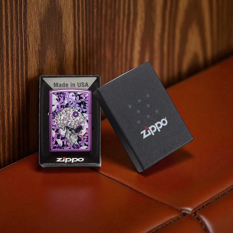 May include: Purple Zippo lighter with a skull design, displayed in its box. The skull is decorated with floral patterns. The box is black with the Zippo logo. The lighter is in a black box that says "Made in USA".