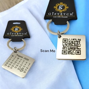 May include: Silver keyring with a black and white QR code and a silver tag with a calendar for August 2020. The tag has a heart symbol on the 19th. The keyring has a black tag with the text "Gifttech Laser Your Moments".