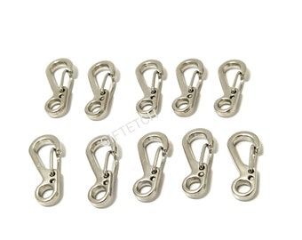 May include: Ten silver-colored spring snap hooks arranged on a white background. Each hook has a curved body with a spring-loaded gate and a circular opening at the base. The hooks are evenly spaced and appear to be made of metal.
