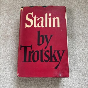 May include: A hardcover book titled "Stalin by Trotsky" with a red cover and white and black lettering. The book's cover is slightly worn, with visible wear and tear along the edges. The title is prominently displayed.