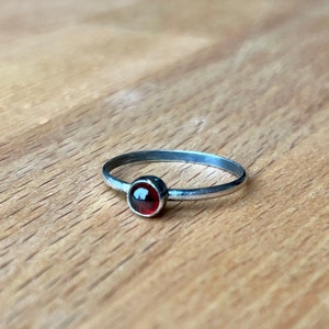 May include: A silver ring with a small, round, red gemstone.