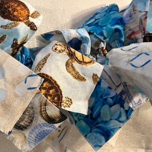 May include: Close-up of fabric squares with a coastal theme. The squares feature sea turtles, seashells, and blue water patterns. The fabric has a light blue and white background with a star pattern.