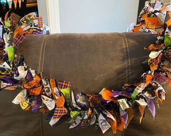 Può includere: Una ghirlanda di Halloween realizzata con ritagli di tessuto in arancione, nero, viola e verde. Il tessuto presenta diversi motivi, tra cui zucche, fantasmi e pipistrelli.