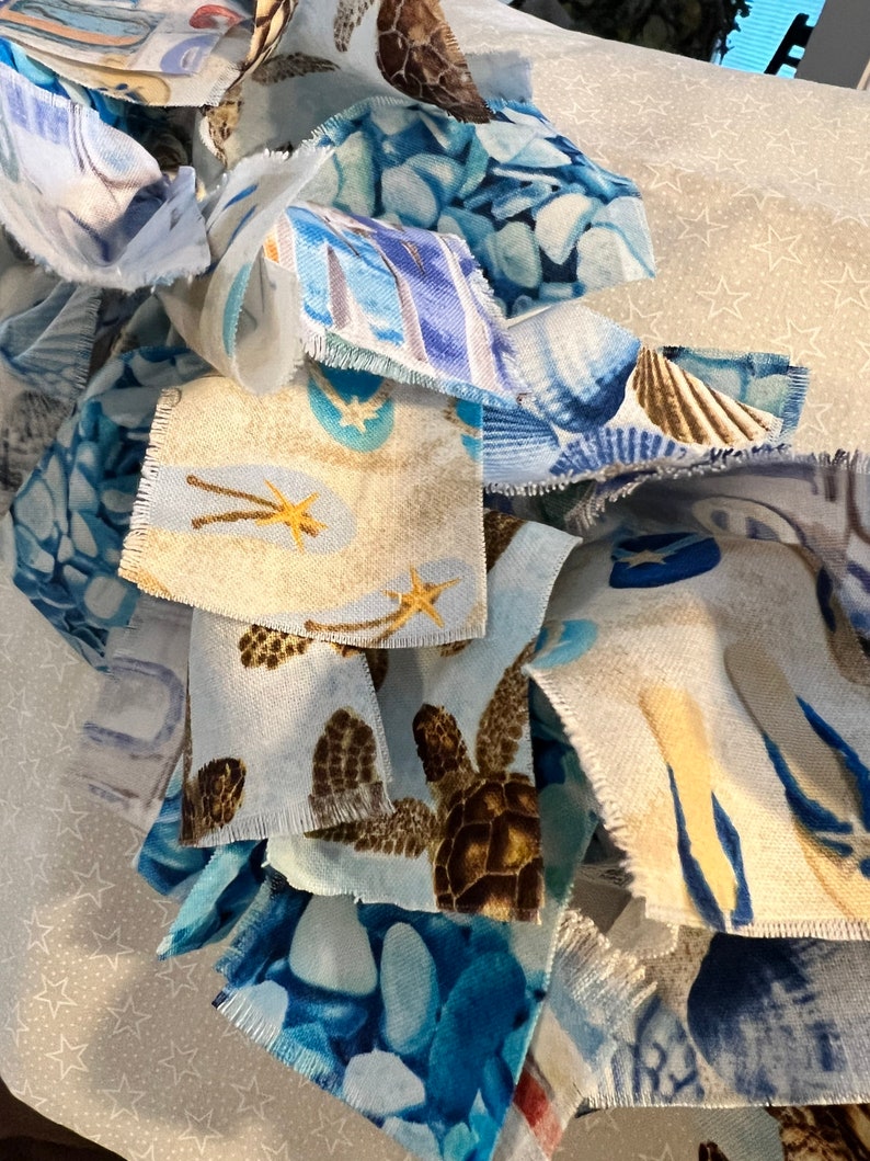 May include: Close-up of fabric scraps with various sea-themed patterns. The fabrics feature images of sea turtles, seashells, starfish, and blue pebble designs. The color palette includes shades of blue, brown, and beige, creating a coastal aesthetic.