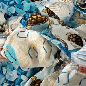 May include: Close-up of fabric pieces with various beach-themed patterns. The designs include sea turtles, seashells, and flip-flops in shades of blue, brown, and white. The edges of the fabric are frayed.
