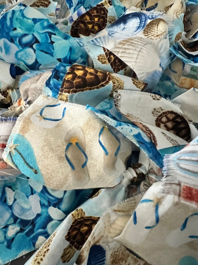 May include: Close-up of fabric pieces with various beach-themed patterns. The designs include sea turtles, seashells, and flip-flops in shades of blue, brown, and white. The edges of the fabric are frayed.