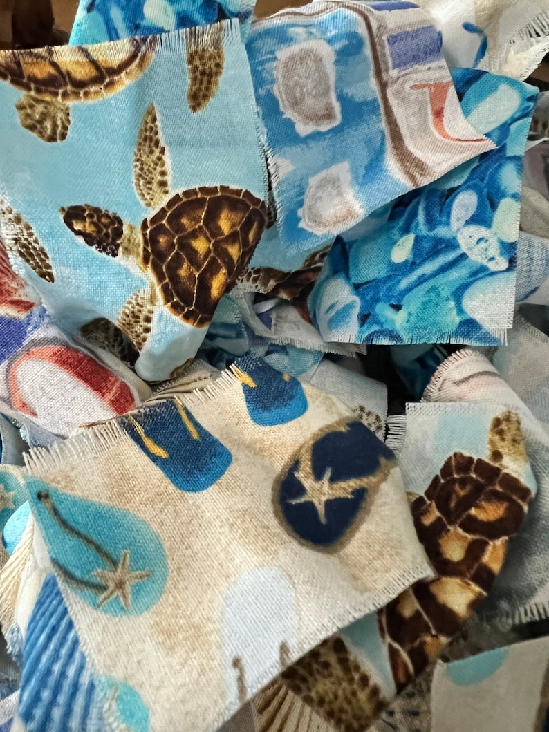 May include: Close-up of fabric scraps with beach-themed patterns. The designs include sea turtles, flip-flops, and starfish in shades of blue, brown, and beige. The edges of the fabric are frayed.