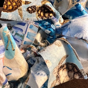 May include: Close-up of a handmade fabric item featuring a repeating pattern of sea turtles in shades of brown, tan, and blue. The fabric has a frayed edge, and the overall design suggests a coastal or nautical theme.