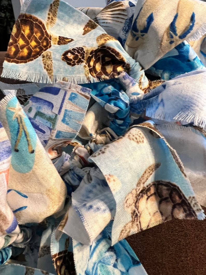 May include: Close-up of a handmade fabric item featuring a repeating pattern of sea turtles in shades of brown, tan, and blue. The fabric has a frayed edge, and the overall design suggests a coastal or nautical theme.