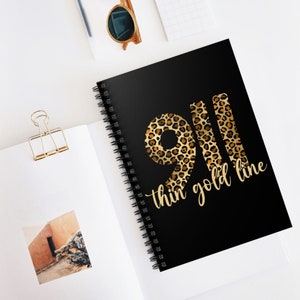May include: Black spiral notebook with a gold and brown leopard print design. The numbers 911 are printed in the leopard print design with the text "thin gold line" below.