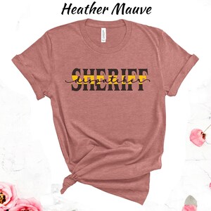 May include: Heather mauve t-shirt with black text that reads "SHERIFF dispatcher" with a yellow and black stripe across the text.