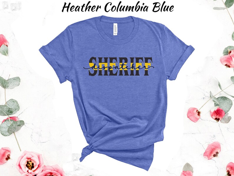 May include: A heather Columbia blue t-shirt with the text "SHERIFF dispatcher" in black lettering with a yellow stripe across the word "SHERIFF".