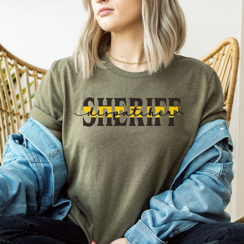 May include: A green t-shirt with the text "SHERIFF dispatcher" in black letters with a yellow and black stripe above the text.