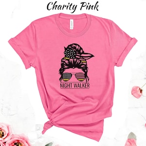 May include: Pink t-shirt featuring a black and white graphic of a woman's hair in a bun with sunglasses and a bandana. The bandana has the American flag design. The text "NIGHT WALKER" is below the graphic.