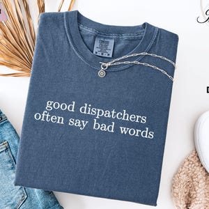 May include: A dark blue t-shirt with the text "good dispatchers often say bad words" printed in white.