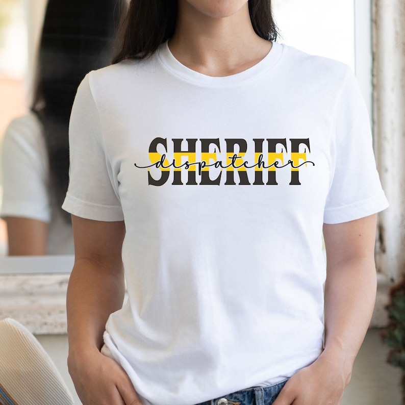 May include: White t-shirt with black text that reads "SHERIFF dispatcher" with a yellow and black stripe above the text.