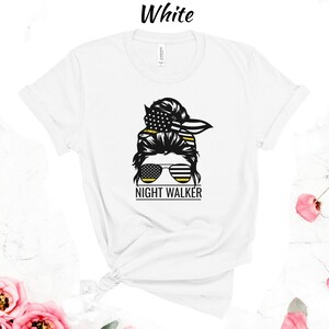 May include: White t-shirt featuring a black and yellow graphic of a woman with a messy bun, sunglasses, and the text "NIGHT WALKER".