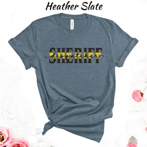 May include: Heather slate blue t-shirt with a black graphic that says "SHERIFF dispatcher" with a yellow stripe across the top of the text.