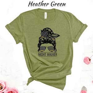 May include: A green t-shirt featuring a graphic of a woman's hair in a bun with an American flag bandana and sunglasses. The text "Night Walker" is below the graphic.