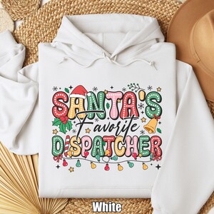 May include: White hoodie with the text "SANTA'S Favorite DISPATCHER" in colorful, festive lettering. The design includes a Santa hat, holly, and a string of lights, perfect for the holiday season. A cozy and cheerful Christmas-themed sweatshirt.