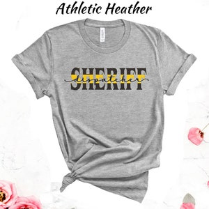 May include: Gray t-shirt with the text "SHERIFF dispatcher" in black lettering with a yellow stripe above the text.