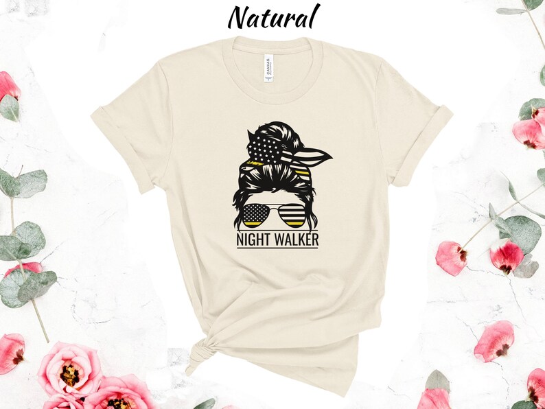 May include: A beige t-shirt featuring a black and yellow graphic of a woman with a messy bun, sunglasses, and the text "NIGHT WALKER".