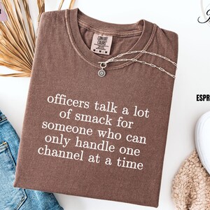 May include: A brown t-shirt with the text "officers talk a lot of smack for someone who can only handle one channel at a time" printed in white.
