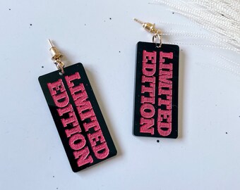 May include: A pair of black acrylic earrings with gold hooks. The earrings are rectangular and have the words "LIMITED EDITION" written in pink on them.