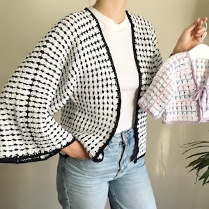 May include: A white and black crochet cardigan with a black trim and a matching smaller cardigan in pink, white, and blue.