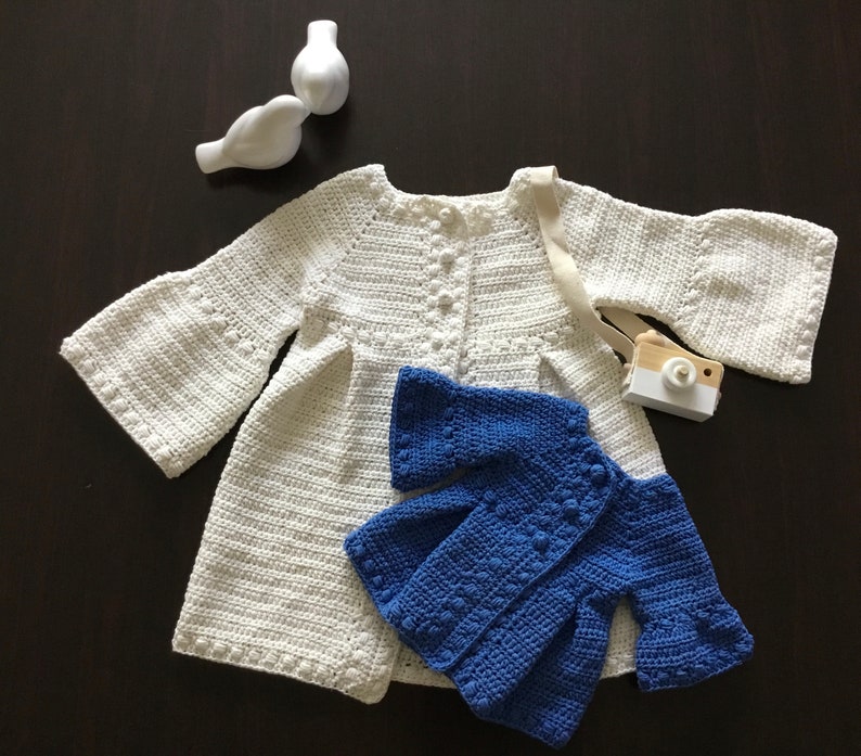 May include: Two crocheted cardigans, one white and one blue. The white cardigan has bell sleeves and a button closure. The blue cardigan has a similar style with a slightly shorter length.