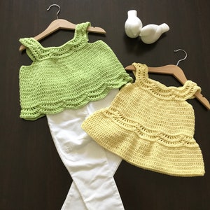 May include: Two crocheted tops, one green and one yellow, with white straps. The tops are laid out on a dark brown surface.
