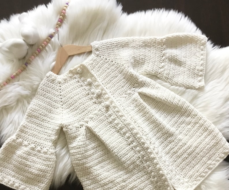May include: A white crocheted cardigan with bell sleeves. The cardigan has a button closure and a delicate stitch pattern.