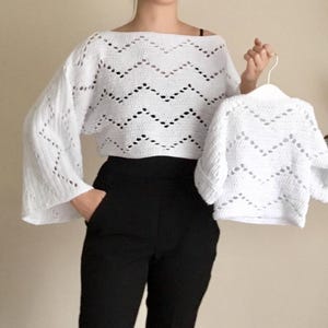 May include: Two white crocheted sweaters with a chevron pattern. The larger sweater has long sleeves and a wide neckline. The smaller sweater has shorter sleeves and a crew neckline.